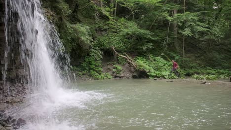 waterfall in the foreground and a water pool with a photographer walking through the bush to set up his tripod