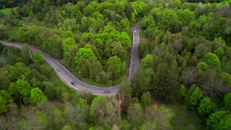 aerial tracking shot of vehicle convoy travelling through lush forest landscape turns down winding road