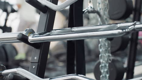 silver chrome cable machine handles and attachments neatly stored on sturdy rack in bright modern gym with blurred windows, cardio machines and weight plates in background showcasing fitness setup