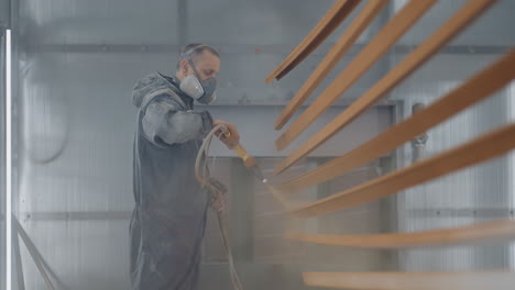 molar sprays paint on steel profiles in a respirator mask and protective suit in slow motion. production and painting studio. general plan