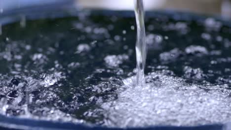 rainwater filling up harvesting barrel, closeup slow motion pouring creating bubbles, slow zoom