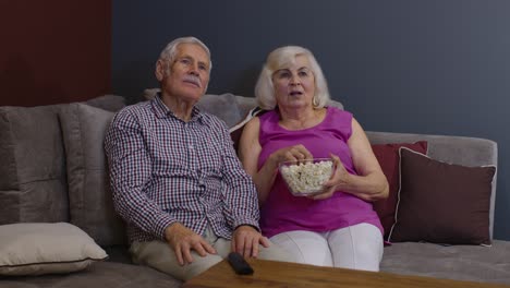 una pareja mayor está disfrutando viendo una película en la televisión y comiendo palomitas de maíz en el sofá en la sala de estar en casa
