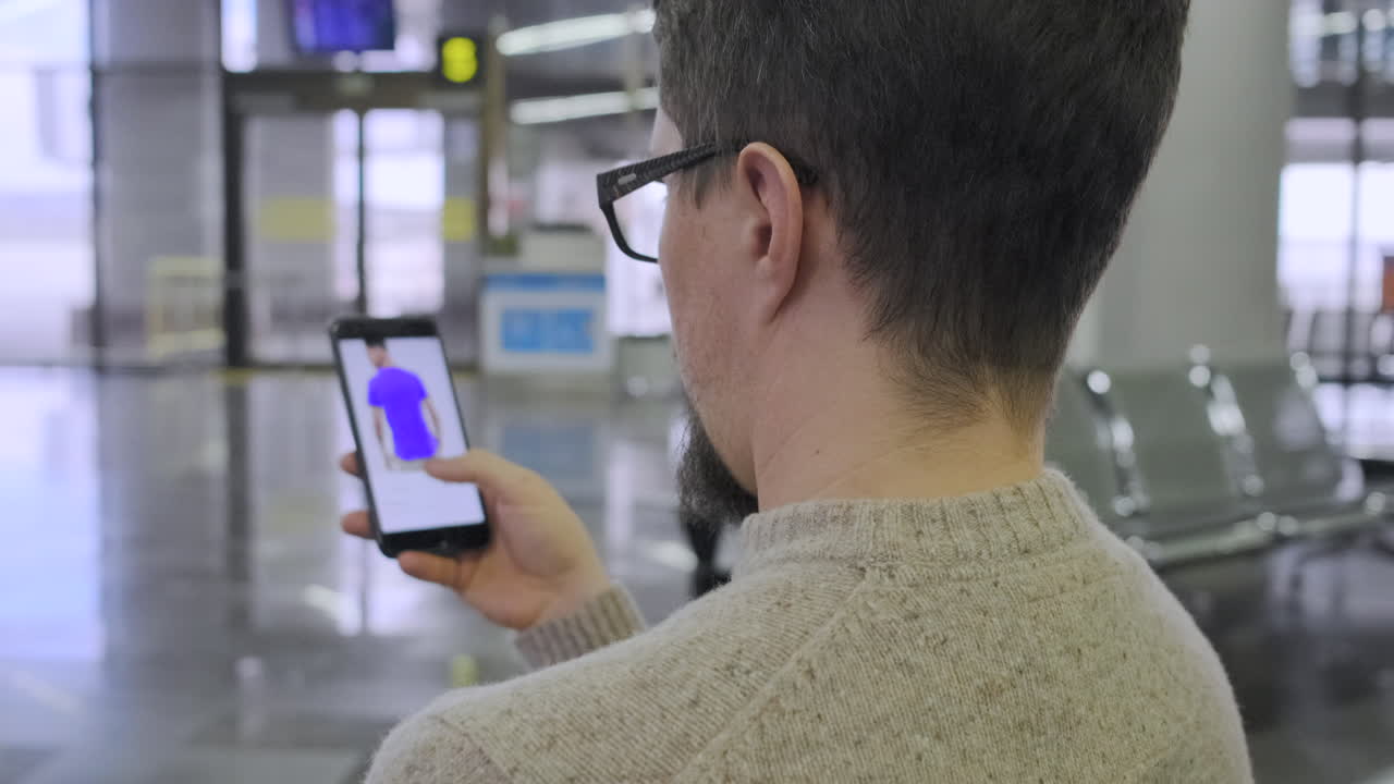 un hombre mirando una tienda de ropa en línea en su teléfono en el aeropuerto.