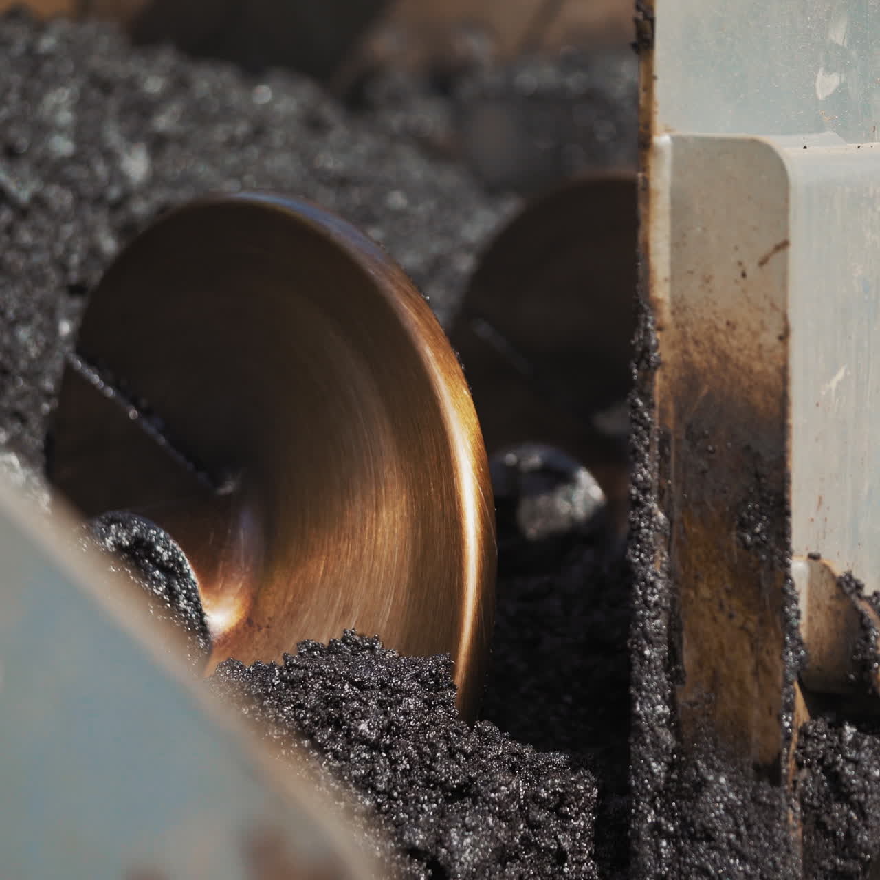 Close-up of hot asphalt pouring out the paver machine to the road. Asphalt paver machine during road construction. Heavy truck laying out black bitumen.