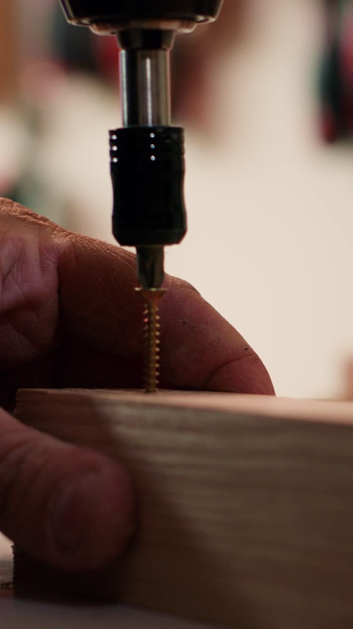 Primo piano di una mano che avvita una vite nel legno con un trapano elettrico