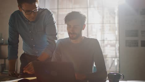 professional creative man sitting at his desk works on a laptop, his colleague helps with poignant advice, they have discussion about decisions made for project. 360 degree tracking arc shot