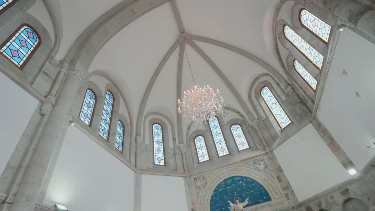 Upward view of elegant church dome with stained glass windows and chandelier inside a historic chapel
