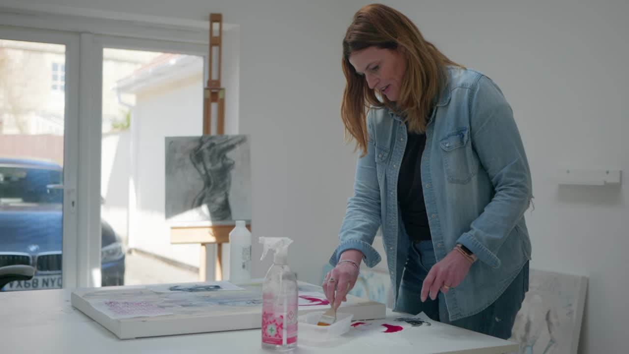 artista femenina cepillando pegamento en un activo de papel, en lienzo, en un estudio en casa