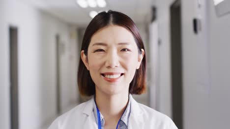 video portrait of smiling asian female doctor standing in hospital corridor