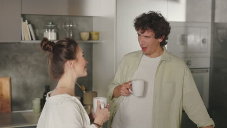 A couple drinking from mugs and interacting in their kitchen