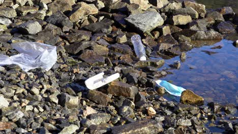 person bends down to pick up plastic garbage on rocky shoreline