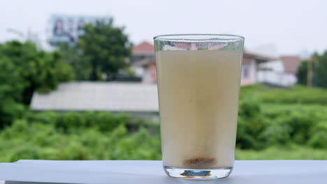 un vaso lleno de agua en el alféizar de la ventana está burbujeando con una tableta de bicarbonato de sodio antiácido dentro de la parte inferior del vaso