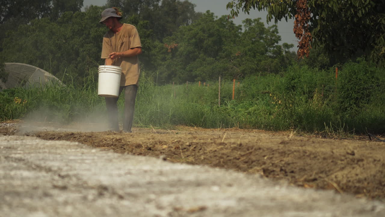 Contadino che sparge fertilizzante sul terreno, concimando il suo campo a mano, concetto di lavoro agricolo