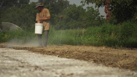 agricultor esparciendo fertilizante en el suelo mientras fertiliza su campo a mano, concepto de trabajo en el campo