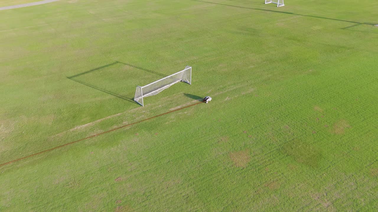 A remote-controlled robot paints precise lines on a soccer field under bright daylight, showcasing automation in sports field maintenance