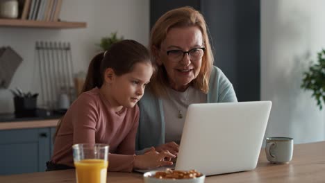 Abuela-Y-Nieta-Caucásicas-Usando-Una-Computadora-Portátil-En-La-Cocina