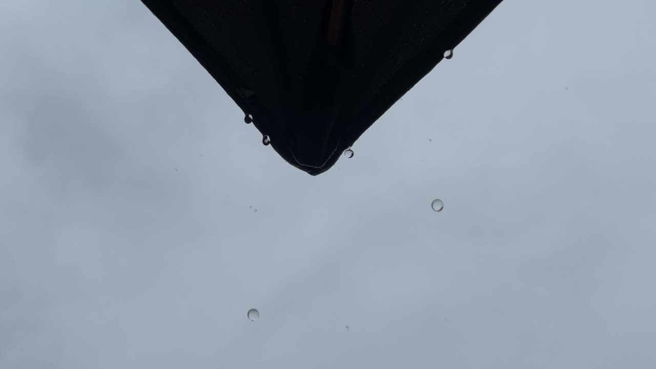 дождь капает с угла зонтика в открытом патио во время ненастной погоды