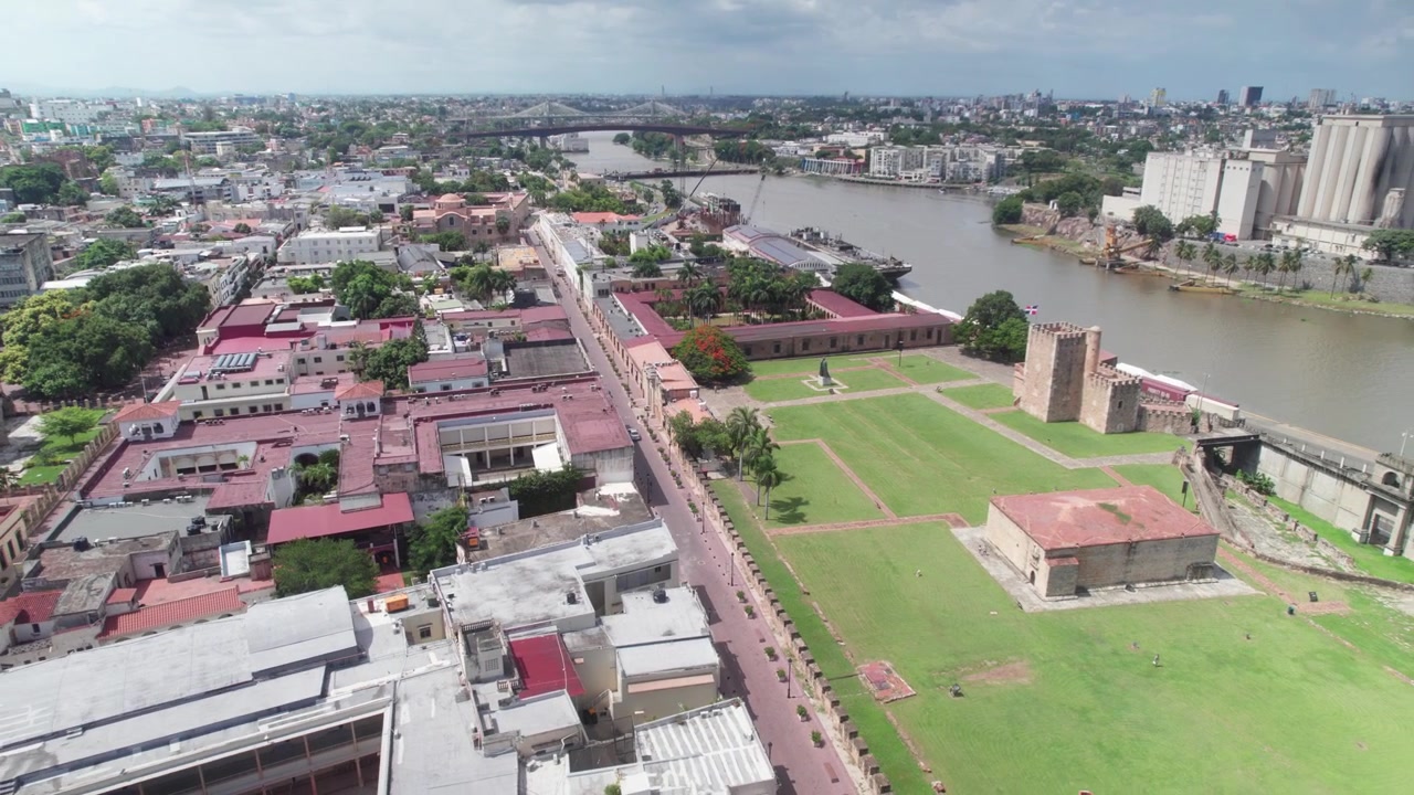 Ripresa aerea con drone del cortile della storica Fortezza Ozama a Santo Domingo, che mostra l'architettura coloniale, gli ampi spazi e il paesaggio urbano fluviale adiacente.