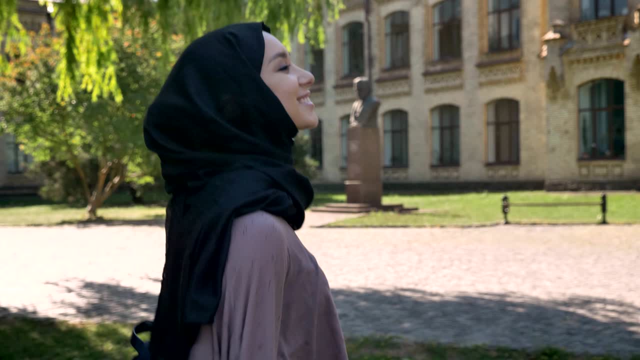 Young sweet muslim girl in hijab is smiling and going to university in daytime in summer, religious concept, studying concept, side view