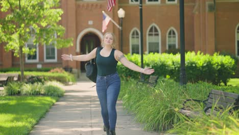 girl wearing backpack jumps for joy and celebrates in front of a college university