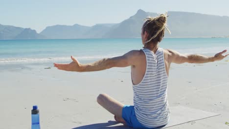 Video-of-rear-view-caucasian-man-with-dreadlocks-practicing-yoga-sitting-on-sunny-beach