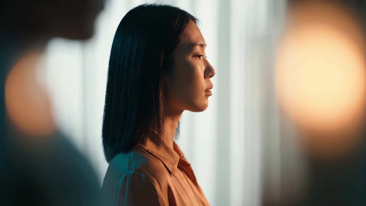 A contemplative moment captured through soft lighting, showing a woman in profile, evoking emotion and reflection amidst blurred backgrounds.