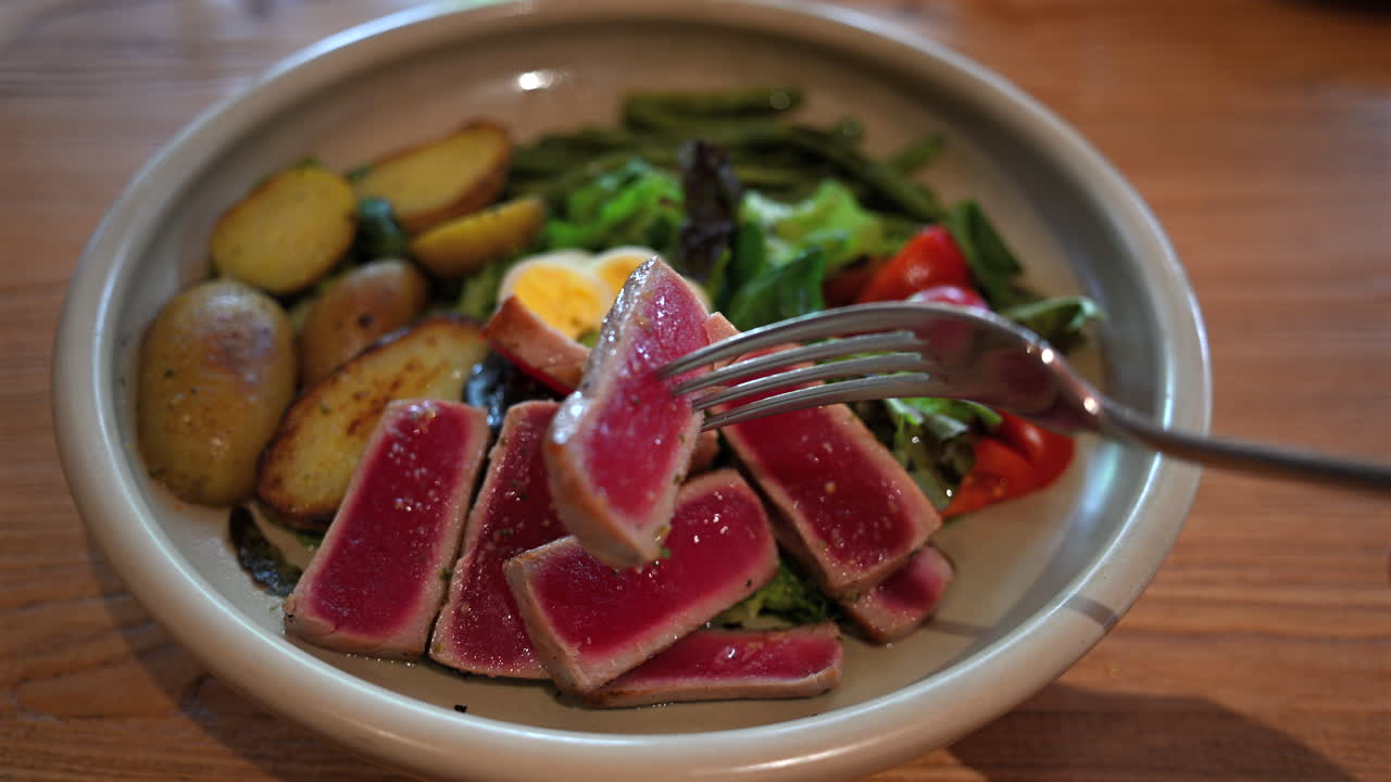 Fresh tuna steak slices served with salad, potatoes, and vegetables