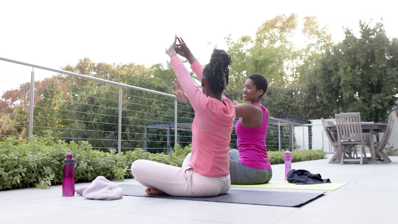 feliz hija afroamericana y madre practicando yoga en el jardín, cámara lenta