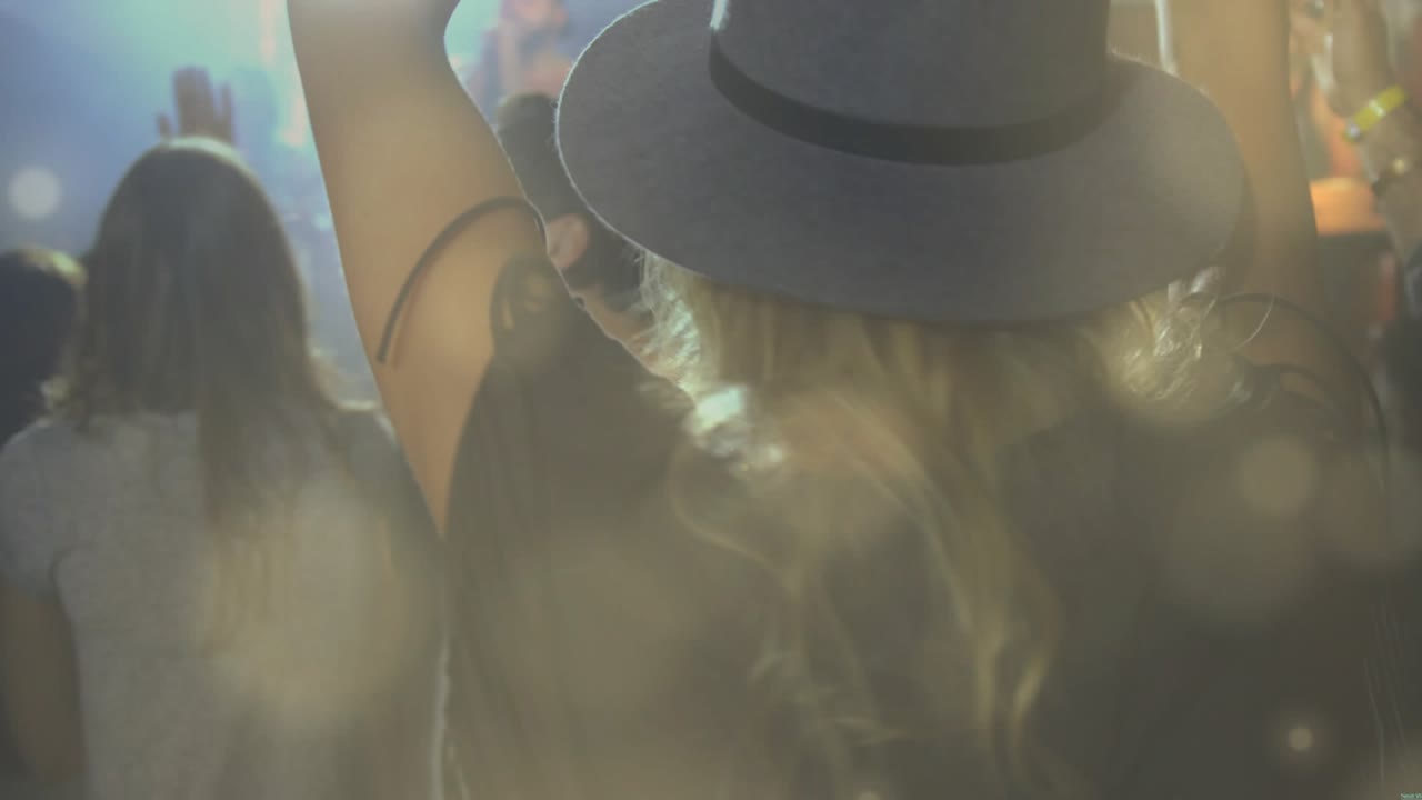 Woman wearing widebrim hat raising arms as artist starting song, stage lights pulsing over concert