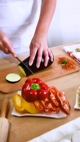 female cook cutting eggplant on wooden board in kitchen.