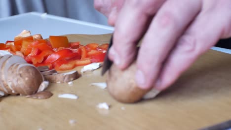 cierre el enfoque superficial en el ingrediente de pimientos rojos picados como manos masculinas, borroso en la chuleta de primer plano - deslice los champiñones nutritivos
