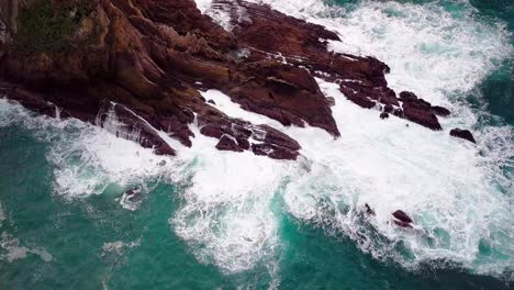 blue ocean waves break on jagged rocks in big sur cali, drone reveal