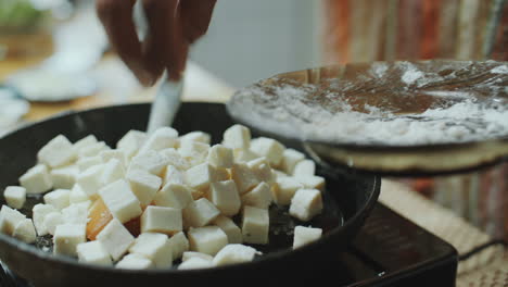 hand of chef adding cubes of paneer cheese to hot pan for cooking