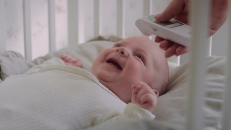 unrecognizable woman measuring temperature to a cheerful baby