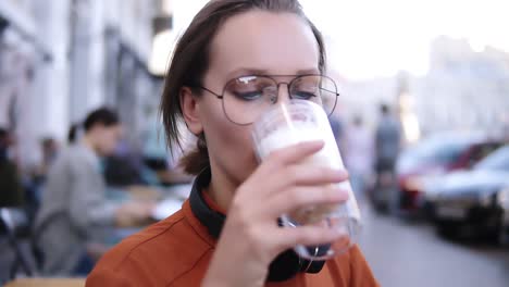 hermosa mujer rubia en una cafetería de verano con gusto beber bebidas con espuma. visitante femenino disfruta tomando sorbos de capuchino de la taza