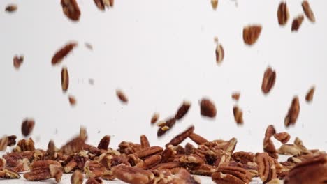 pecan nut pieces raining down onto white table top and bouncing into a pile in slow motion