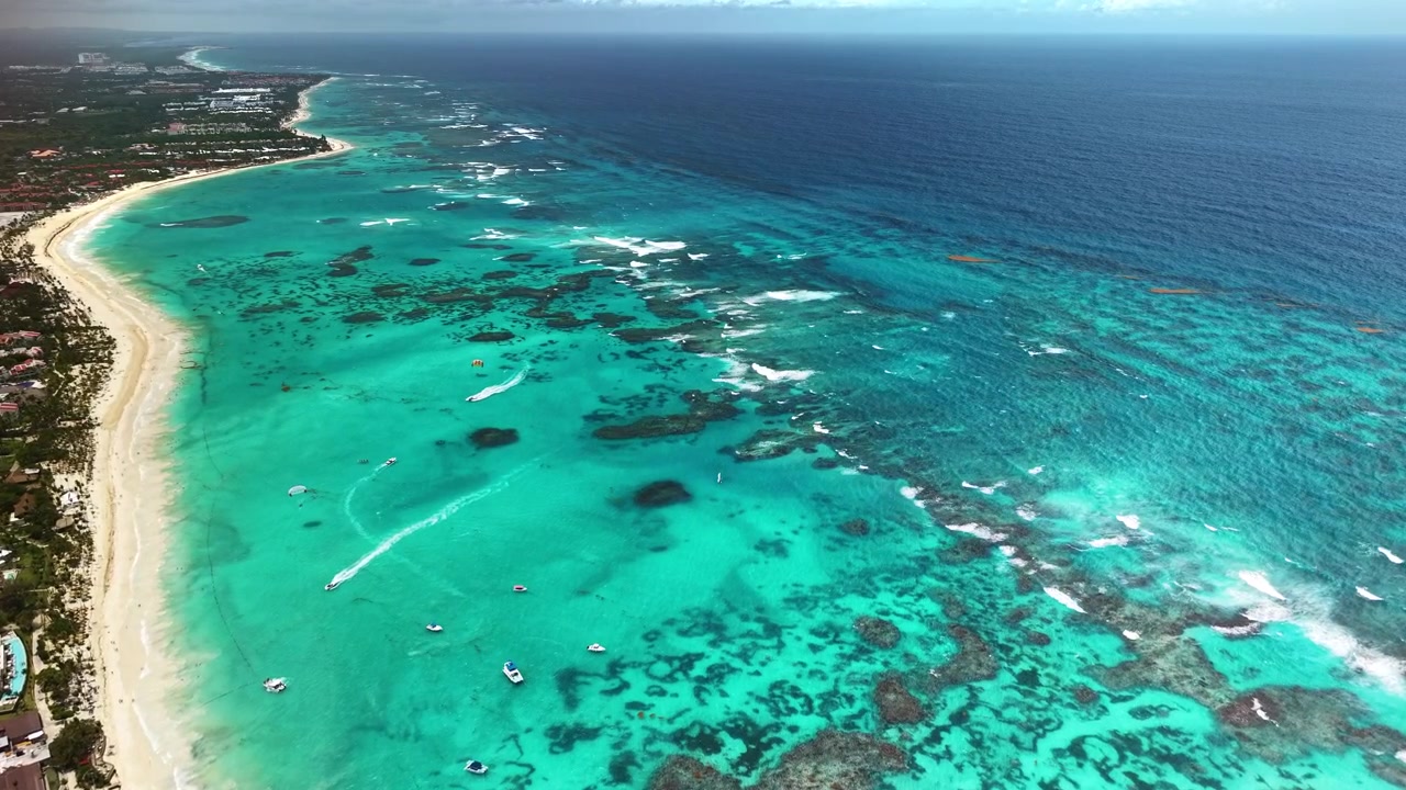 Veduta aerea con drone di una lunga spiaggia bianca con bassi fondali turchesi, una barriera corallina e piccole imbarcazioni, Punta Cana, Repubblica Dominicana