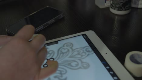 la mano de una mujer que es una artista del tatuaje dibuja un diseño de attoo en una tableta para prepararse para el tatuaje