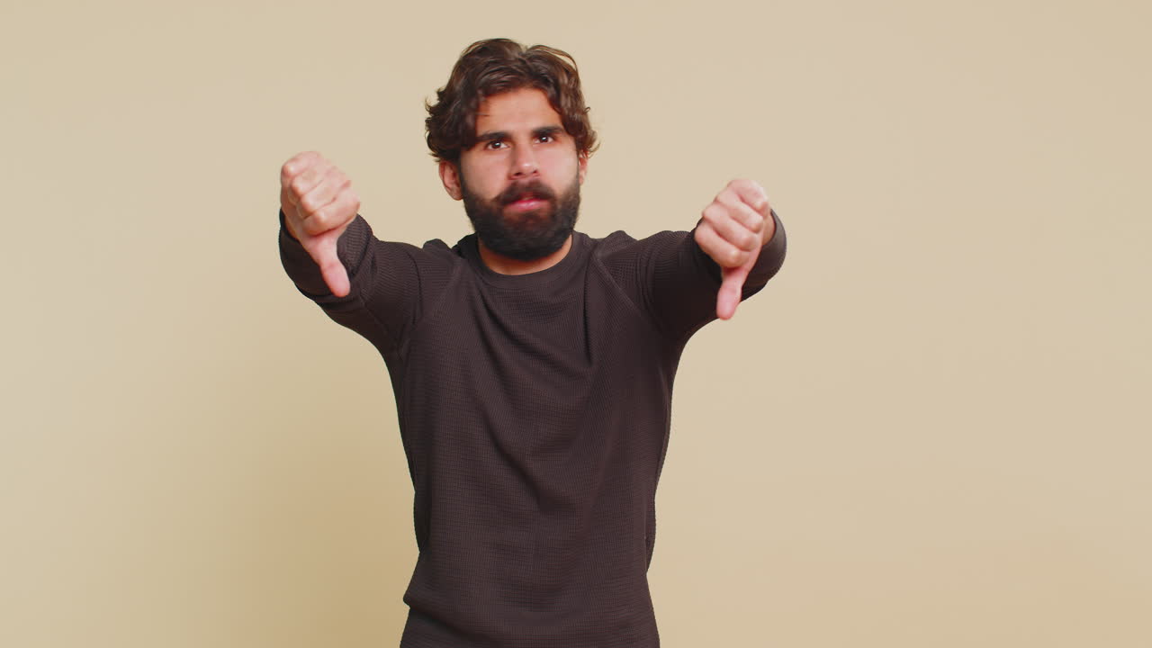 Upset unhappy lebanese man in long sleeves showing thumbs down sign gesture against beige background