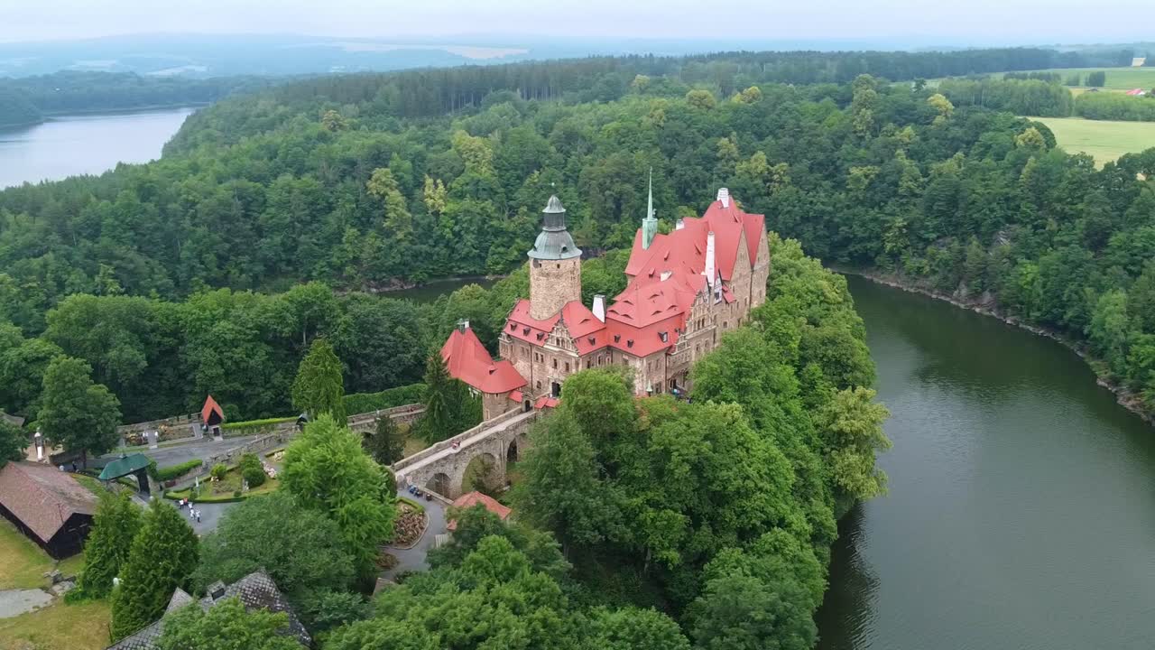 Aerial flyover of fairytale-style Czocha Castle in Poland surrounded by forest and lake