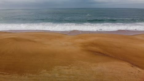 Aerial-View-Of-Nazare-Waves-Breaking-On-Orange-Sandy-Beach