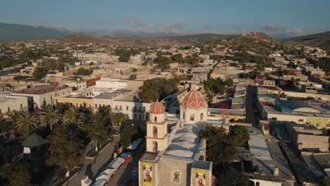vista aérea de una iglesia en una tranquila ciudad mexicana al anochecer con la colina verde en el fondo