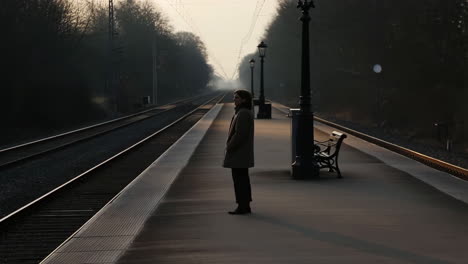 a lone person standing on a train station platform at sunrise or sunset