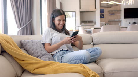 sitting on couch, teenage girl smiling while using smartphone, relaxing at home