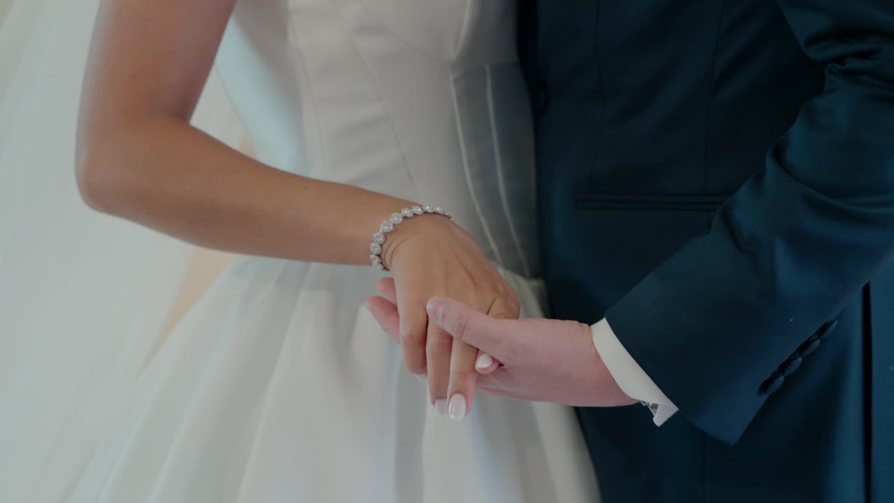 Elegant bride in white gown and groom in navy suit holding hands lovingly