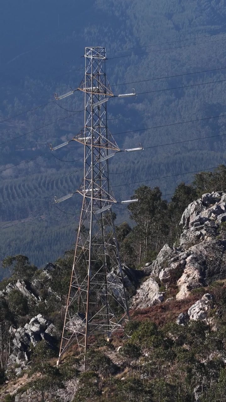 Drone shot of energy power lines and high voltage towers across the mountains.