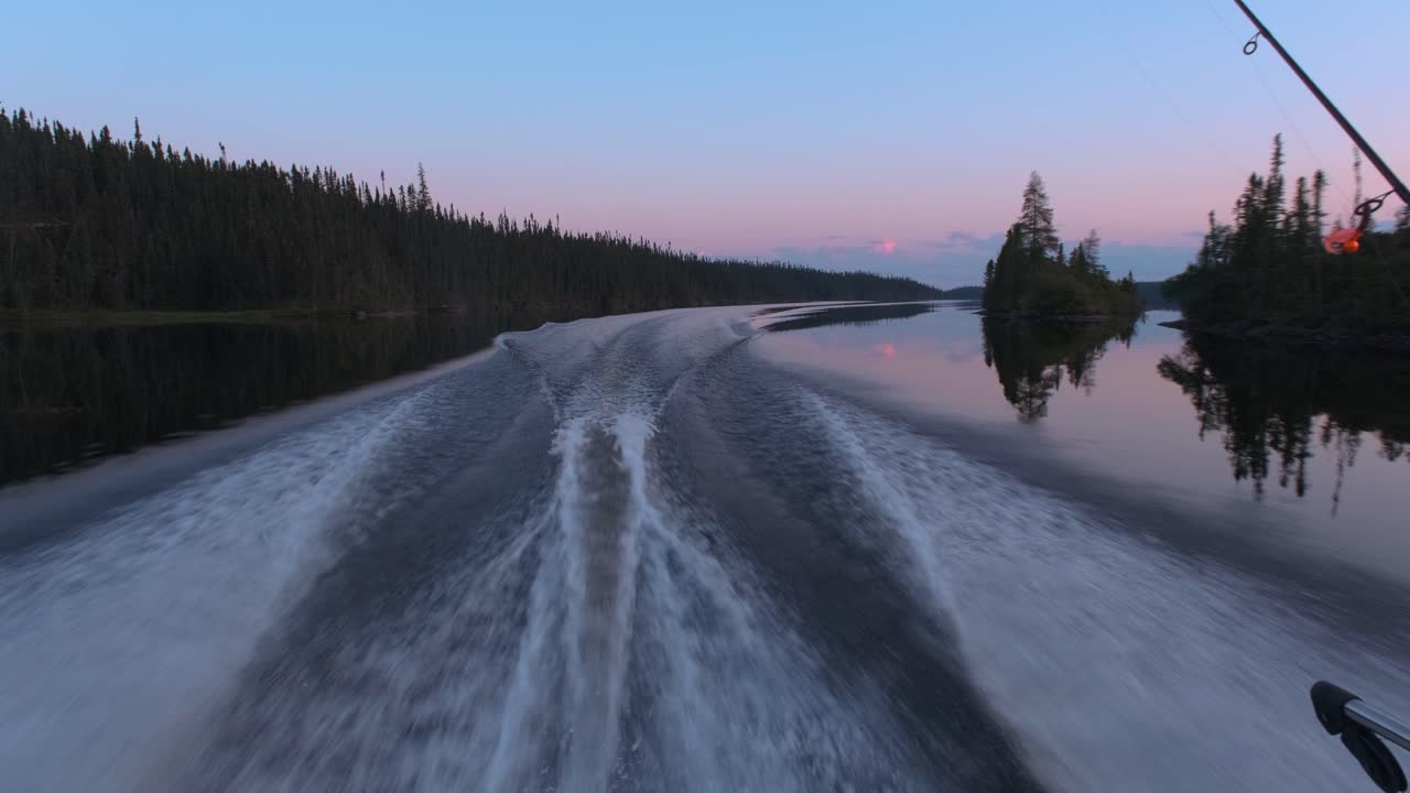 Back view of a fishing boat sailing quickly on a beautiful lake at sunset