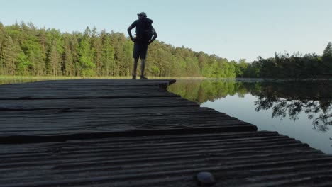 man wearing large backpack walks to edge of pier dock to stop and take in the hiking views