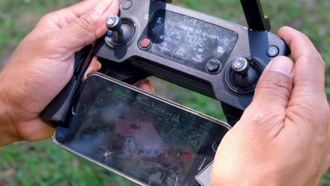 piloto de drones que vuela un drone usando un controlador de drones y una pantalla de teléfono móvil, cerca de las manos que operan equipos de cámara