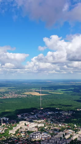 panoramic view of a city among green nature. cityscape under blue sky with white clouds. beautiful scenery of a town near fields. aerial view. vertical video